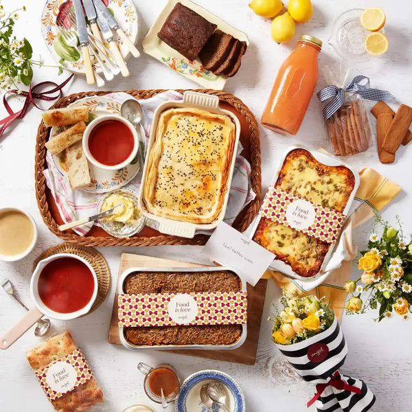 Selection of baked dishes, soup, and juice arranged in a basket with Angel Delivery cards