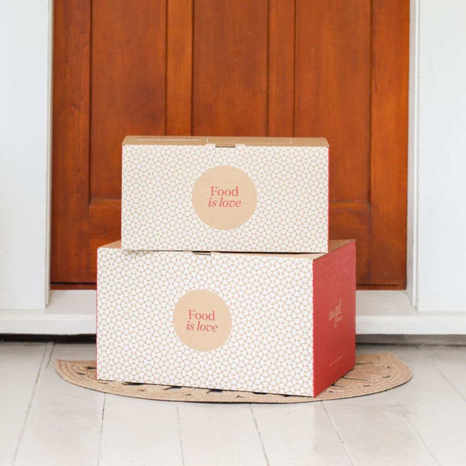 Two “Food is love” delivery boxes stacked at a doorstep in front of a wooden door.