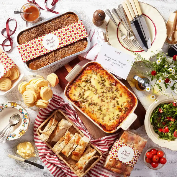 Baked meals, cookies, bread, and salad with Angel Delivery note on a white table