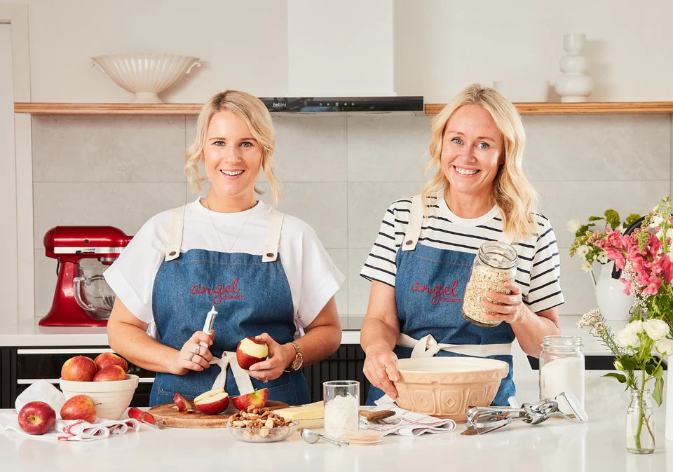 Two women preparing apples and oats in a kitchen wearing Angel Delivery aprons