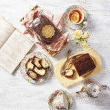 Baked loaf cake with slices buttered on floral plates, served with tea, flowers, and a vintage recipe book.