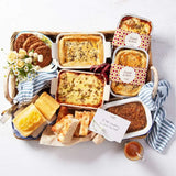 Food hamper with lasagna, pies, lemon cake, bread, cookies, and a gift card arranged in a basket.